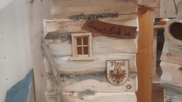 A rustic wooden house with a small window and a sign saying "Grias Eich". Next to the window is the coat of arms of Tyrol.