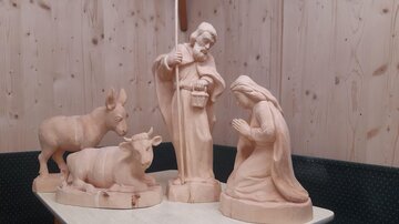 A wooden nativity scene with figures of Mary, Joseph, and animals. The sculptures are simple and in a natural color tone.