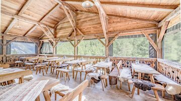 A cozy interior with wooden furniture and large windows. The room is bright and inviting, ideal for social gatherings.