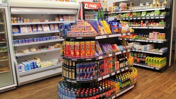 A well-organized grocery store with shelves full of snacks, drinks, and canned goods. On the left side, there is a freezer with various dairy products.