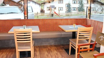 A cozy interior with modern tables and chairs. The large windows offer a view of the surrounding buildings and landscape.