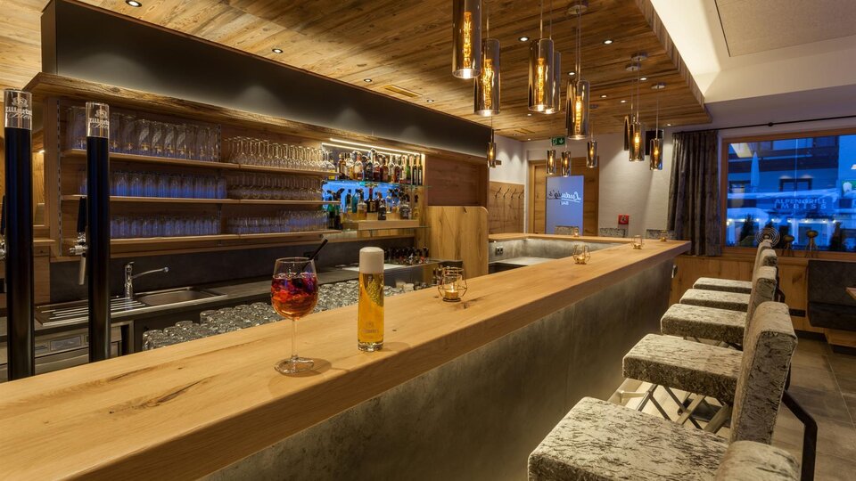 A modern bar with wooden decor and elegant lighting. In the background, there are glasses and a selection of drinks.