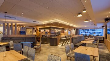 A modern restaurant with wooden details and cozy tables. The lighting creates an inviting atmosphere.