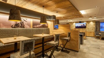 A modern restaurant with wooden elements and cozy lighting. The seating areas are inviting and contemporarily designed.