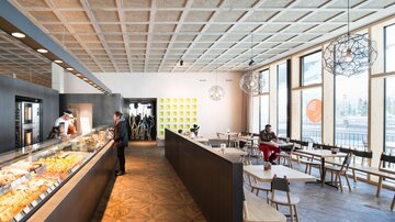 A modern restaurant with an airy atmosphere. Various foods and drinks are available at the counter, while guests sit at table groups. | © MPREIS Warenvertriebs GmbH