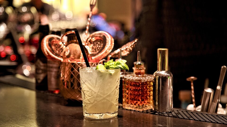 A delicious cocktail with fresh mint is on an elegant bar. In the background, various bottles and utensils are visible.