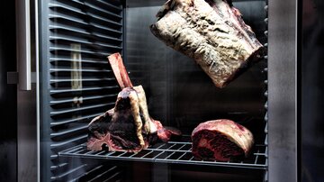 A refrigerator with various cuts of meat for the aging process. The meat is clearly visible and displays different cuts.
