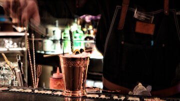 A bartender is preparing a cocktail in a stylish bar. In the background, various drinks in vivid colors can be seen.