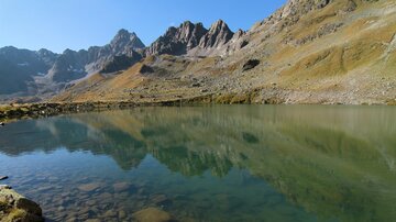 A tranquil lake, surrounded by impressive mountains. The clear water reflects the landscape.