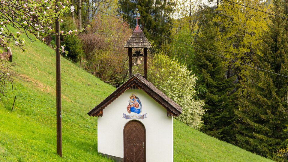 A small chapel stands on a green meadow. Surrounded by trees, it conveys a quiet and idyllic atmosphere.