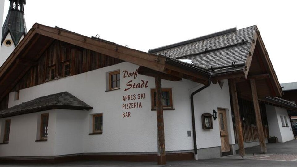 A cozy restaurant with wooden paneling, known for après-ski. The facade displays the name "Dorf Stadl" and invites you to linger.