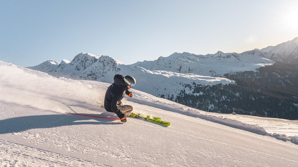 A skier glides over a snowy slope in the mountains. In the background, impressive mountain landscapes can be seen.