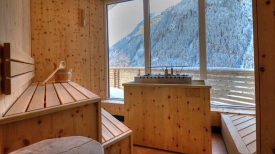 A cozy wellness area made of wood with a view of snow-covered mountains. Light streams through large windows, creating a relaxing atmosphere.