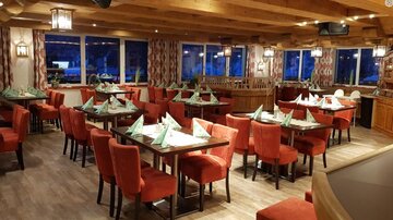 A cozy restaurant with red chairs and green napkins on the tables. The large windows offer a view of the surroundings.