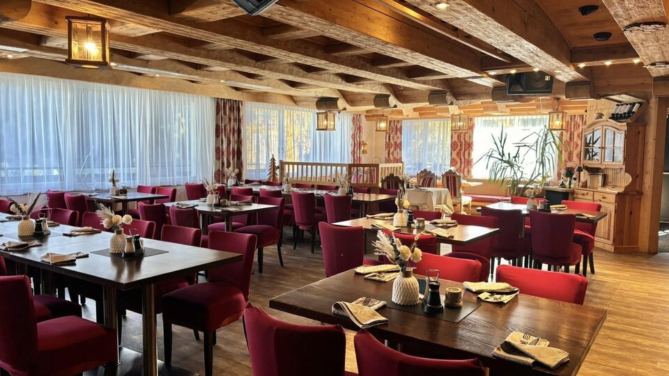 A cozy restaurant with wooden elements and red chairs. The tables are set warmly and the windows offer a view outside.