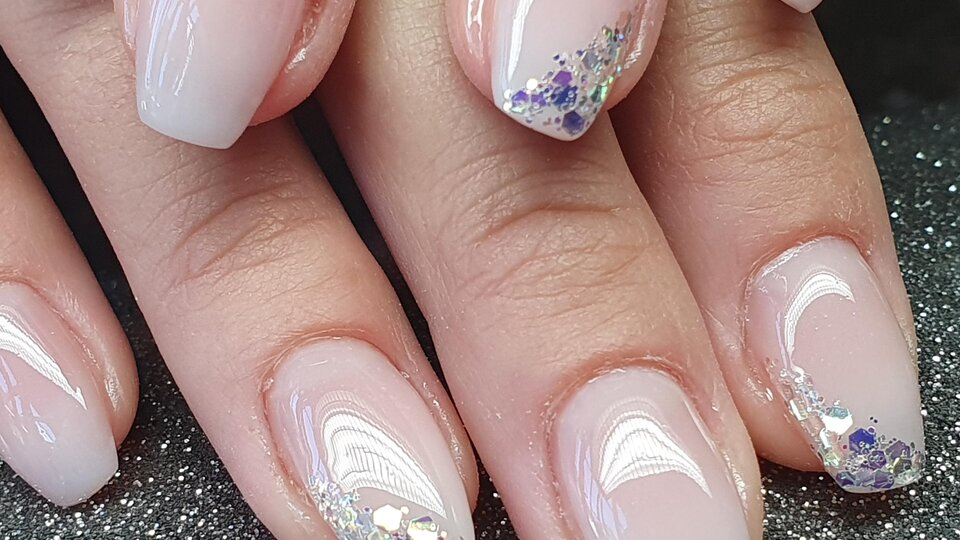 Schöne Maniküre mit zarten, rosafarbenen Nägeln und glitzernden Akzenten. Die Nägel sind sauber geformt und glänzen elegant.