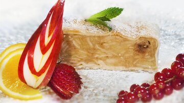 A delicious piece of apple strudel, garnished with fresh fruits and a mint leaf. Delicate pastry and a sweet filling make the dessert appealing.