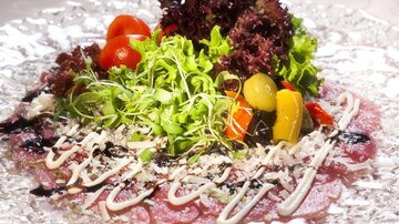A attractively arranged carpaccio with fresh vegetables, salad, and special sauces. The presentation is colorful and inviting.