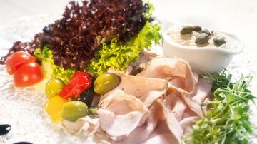 A plate with cold cuts, fresh vegetables, and a dip. The colorful selection includes salad, olives, and tomatoes.