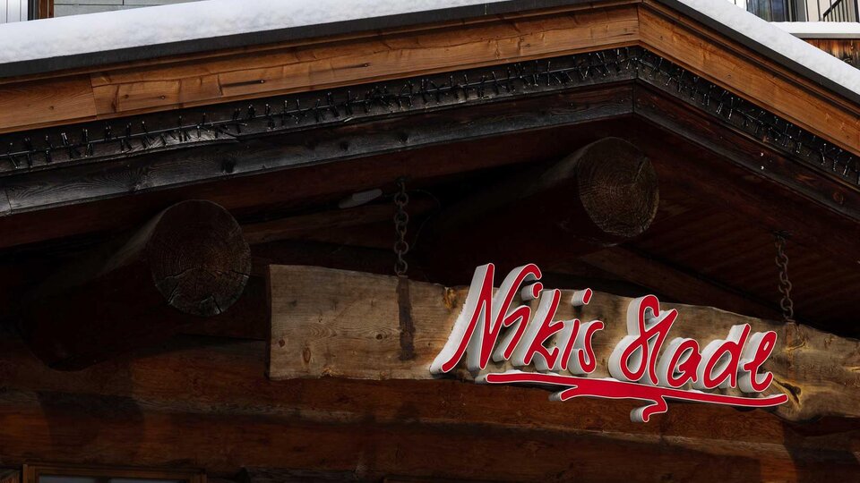A traditional wooden building with a snow-covered roof. The sign reading "Nikis Stube" is clearly visible.