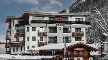 A modern hotel in the snow, surrounded by mountains. The entrance area features inviting wooden architecture.