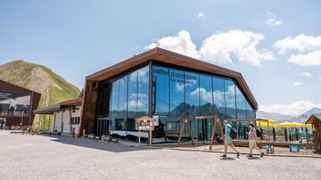 A modern building with large window areas in the mountains. In front of the building are recreational facilities and a clear view of the surroundings.