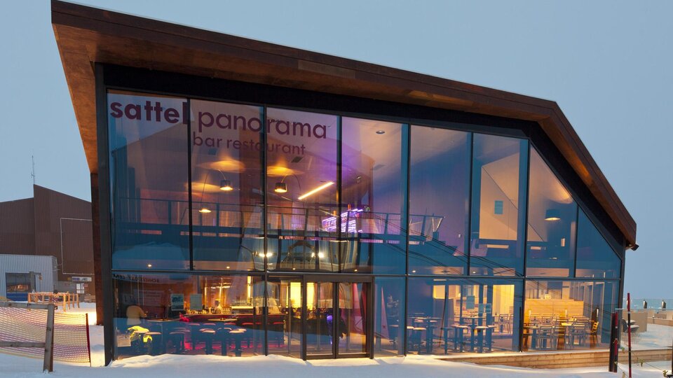 A modern restaurant with large glass windows and a simple wood design. The building is located in a winter setting with snow.