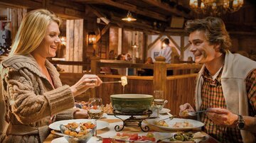 A cozy restaurant with a couple enjoying fondue. Various foods are on the table and a warm, inviting atmosphere.