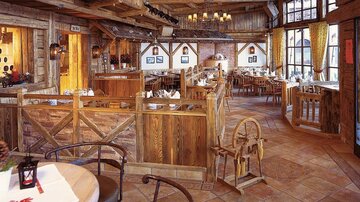 A cozy wooden-style restaurant with rustic furniture and warm lighting. Large windows offer a view outside and create an inviting atmosphere.