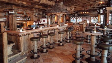 A rustic bar in a cozy restaurant with wooden interior. There are high tables and chairs that create an inviting atmosphere.