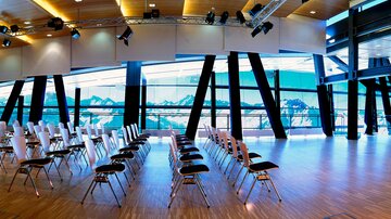 Ein moderner Konferenzraum mit leeren Stühlen und großen Fenstern. Der Blick reicht auf beeindruckende Berglandschaften.