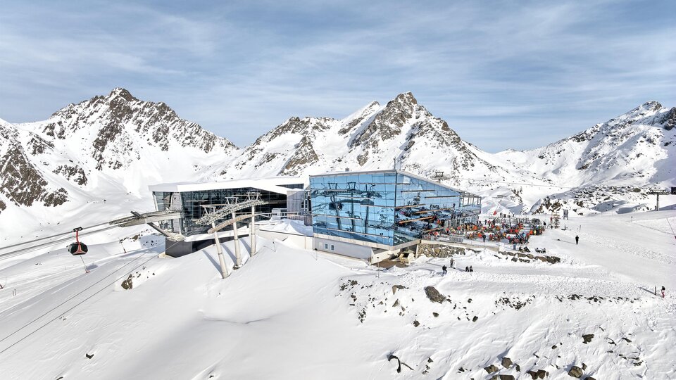 Eine moderne Bergstation in den verschneiten Alpen. Im Hintergrund sind majestätische Berge und ein klarer Himmel zu sehen.