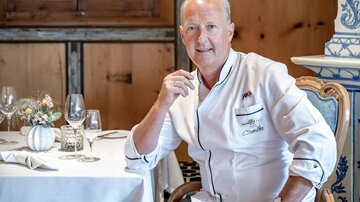 A chef in an elegant restaurant setting is sitting at a table. The room is cozy and stylishly furnished.