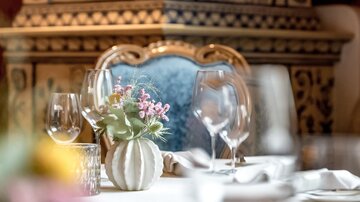 An elegant table arrangement with glasses and a small flower vase. In the background, an artistically decorated stove can be seen.