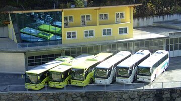 A modern bus stop with several yellow and white buses. In the background, there is a yellow building with large windows.