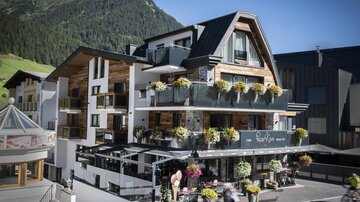 A modern hotel with blooming balcony plants in a mountain landscape. The facade is friendly and inviting.