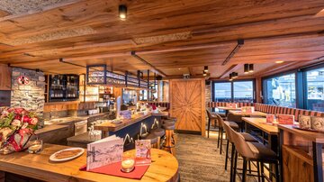 A cozy restaurant with wooden decor and an inviting bar. Large windows offer a beautiful view of the surroundings.
