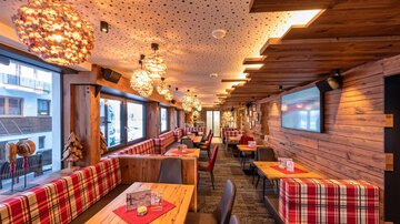 A cozy restaurant with wooden decor and rustic tables. The walls are equipped with windows that let in a lot of light.