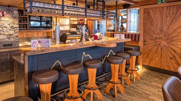 A cozy bar with wooden chairs and an inviting counter. The space has a warm atmosphere and is tastefully furnished.