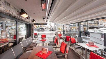 A modern café with elegant tables and red chairs. Large windows provide a view of the surroundings.