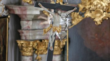 A crucifixion depiction with a figure of Jesus on the cross. In the background, elaborate golden and marbled elements are visible.