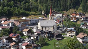 A picturesque mountain town with traditional houses and a distinctive church. Surrounded by green meadows and dense forests.