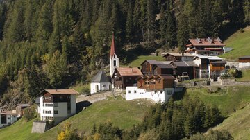 A picturesque village in the mountains, surrounded by green meadows and tall trees. The church with the distinctive tower is an eye-catcher in the landscape.