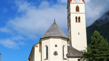 Eine schöne Kirche mit einem roten Turm und einer weißen Fassade. Im Vordergrund befindet sich ein modernes Gebäude mit einem Glasbereich.