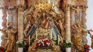 Ein prachtvoller Altar mit einer Statue der Madonna, umgeben von Engeln und Blumenschmuck. Die goldenen Verzierungen und die detailreiche Darstellung schaffen eine feierliche Atmosphäre.