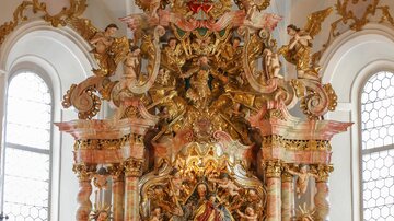 Ein prächtiger Altar in einer Kirche, reich verziert mit Gold und Statuen. Blumen schmücken den Altar und schaffen eine feierliche Atmosphäre.