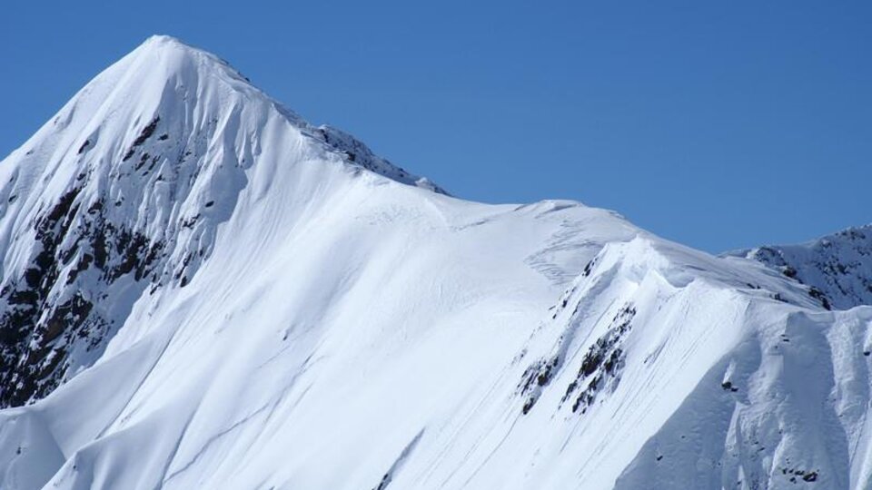 A snow-covered mountain under a clear blue sky. The landscape is majestic and impressive.