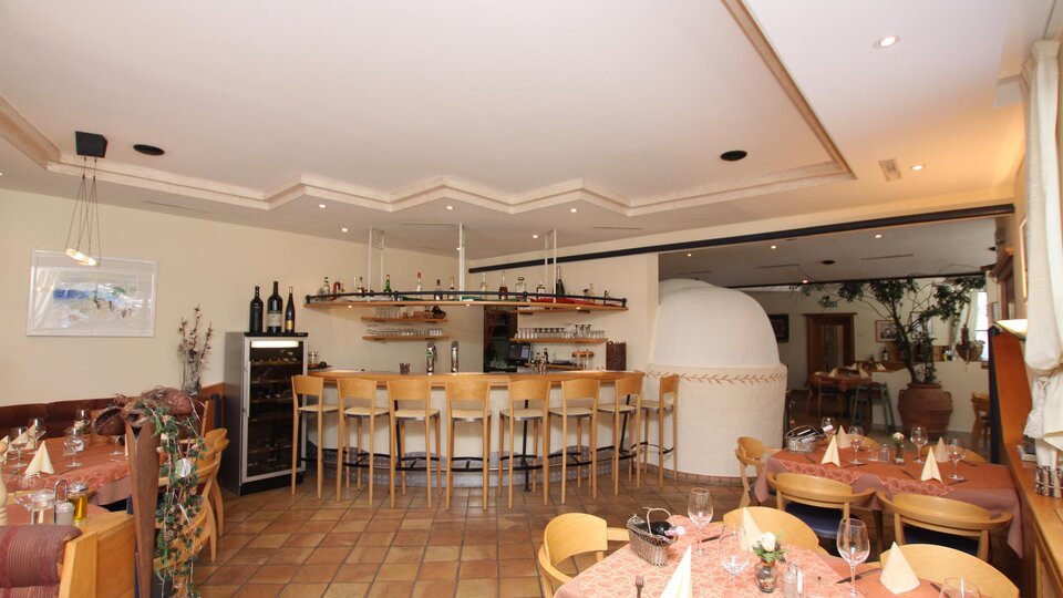 A cozy restaurant with a bar and wooden furniture. The tables are elegantly set and there is a beautiful indoor area.