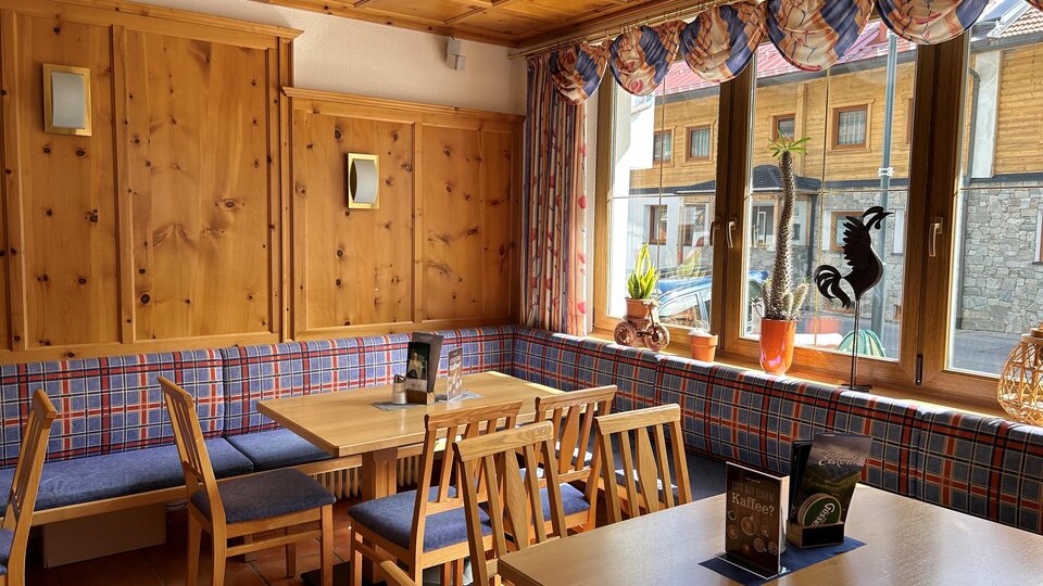A cozy restaurant with wooden furniture and checkered upholstery.  
Large windows let in plenty of light and offer a view outside.