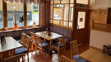 A cozy restaurant with wooden furniture and large windows. The room is bright and inviting, perfect for social conversations.